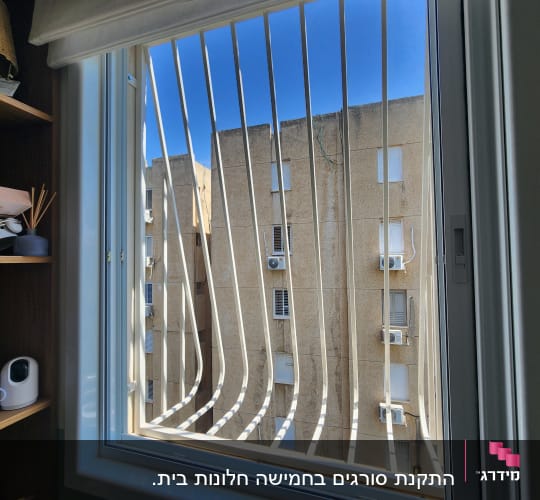 חלון עם סורגים לבנים מול בניין חיצוני